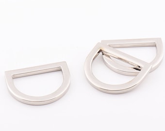 May include: Four silver metal D-rings, also known as D rings or D-shaped rings, are stacked on top of each other. The rings are smooth and shiny.