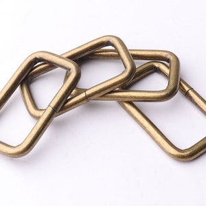 May include: Four antique gold-toned metal D-rings, stacked on top of each other. The rings are rectangular with rounded corners.