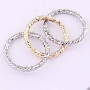 Puede incluir: Tres llaveros de metal con un diseño de cuerda trenzada. Los anillos son plateados, dorados y plateados.