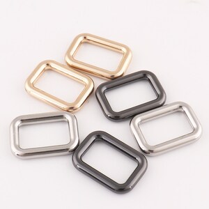 Puede incluir: Cinco anillas en D de metal en diferentes acabados: dorado, plateado y negro. Las anillas son rectangulares con esquinas redondeadas.