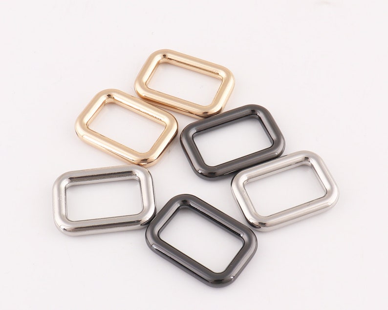 Puede incluir: Cinco anillas en D de metal en diferentes acabados: dorado, plateado y negro. Las anillas son rectangulares con esquinas redondeadas.