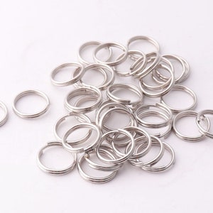 Op de afbeelding: Een stapel zilverkleurige metalen sleutelringen. De sleutelringen zijn allemaal even groot en even gevormd, en ze zijn in een willekeurig patroon gerangschikt.