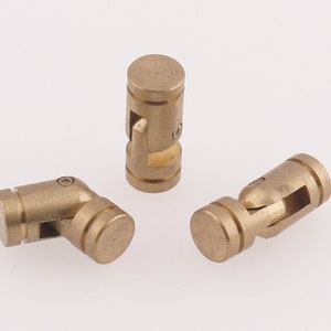 Puede incluir: Tres juntas universales de metal de color dorado, cada una con forma cilíndrica y una junta esférica central giratoria. Las juntas están diseñadas para permitir un movimiento flexible en múltiples direcciones.