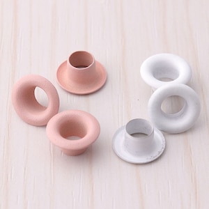 Könnte beinhalten: Sortiment aus Metallösen in Rosa und Weiß. Die Ösen sind in verschiedenen Größen und eignen sich ideal für Bastelprojekte.