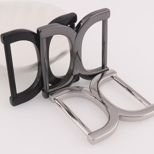 May include: Three metal belt buckles in different finishes. The buckle on the bottom is silver, the middle buckle is black, and the top buckle is a darker shade of silver.