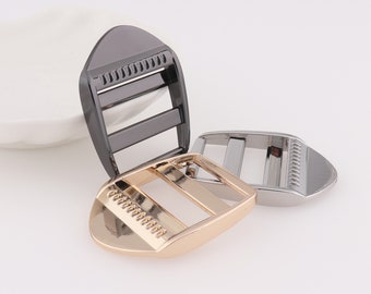 May include: Three metal slider buckles in different finishes: black, silver, and gold. Each buckle has a rectangular shape with a smooth, polished surface and a textured edge.