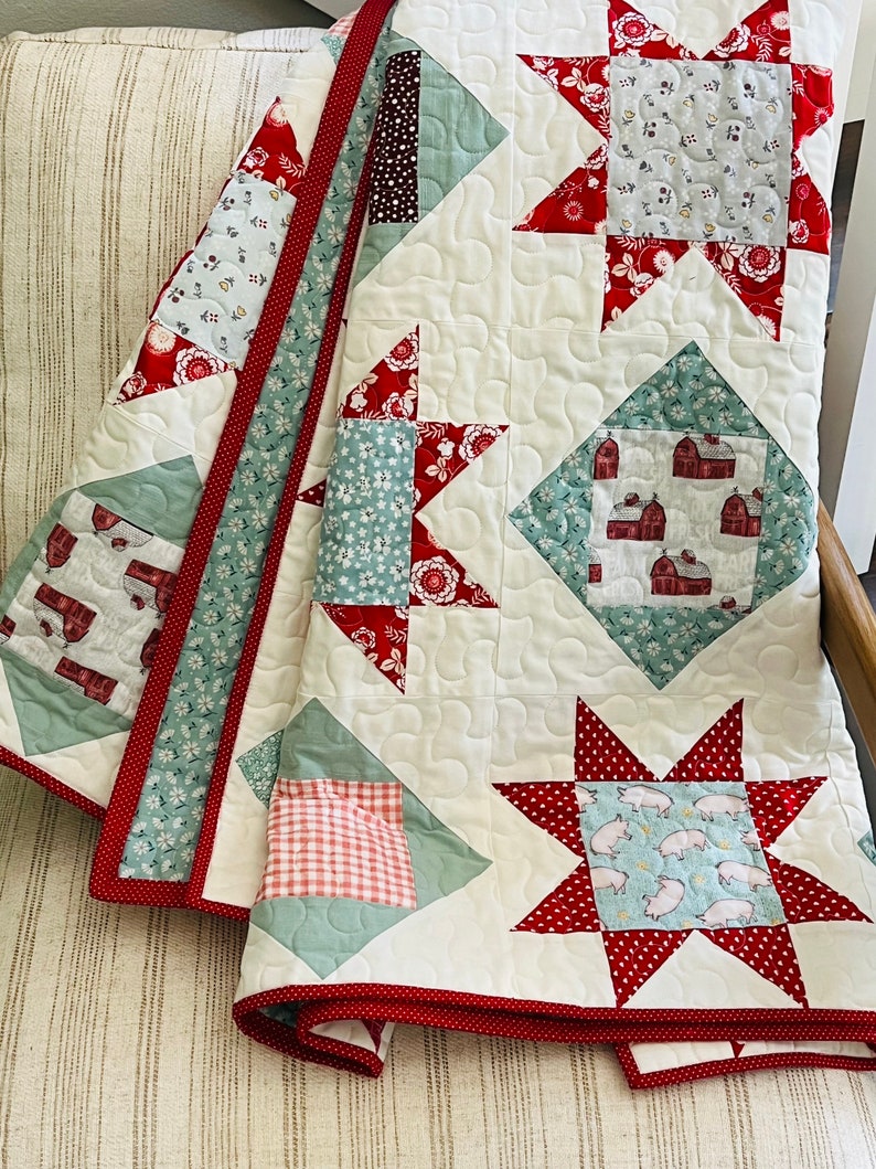 May include: A white quilt with a red and green patchwork design. The quilt features a variety of patterns, including stars, squares, and diamonds. The quilt is edged with a red trim.