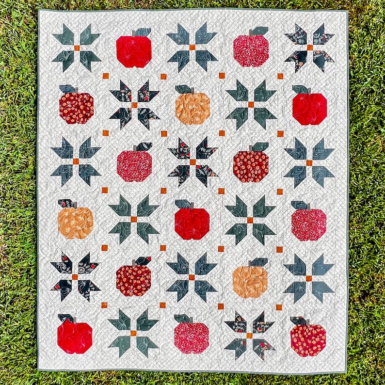 Puede incluir: Una colcha blanca con un patr&oacute;n repetido de manzanas rojas y bloques en forma de estrella en blanco y negro. La colcha est&aacute; hecha con una variedad de telas y texturas.