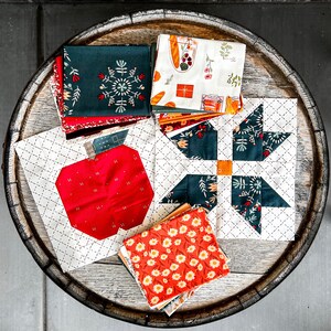 Puede incluir: Una colecci&oacute;n de cuadrados de tela con varios patrones y colores, incluyendo rojo, verde, blanco y negro. Las telas est&aacute;n dispuestas sobre una superficie de madera y presentan dise&ntilde;os como manzanas, estrellas y motivos florales.