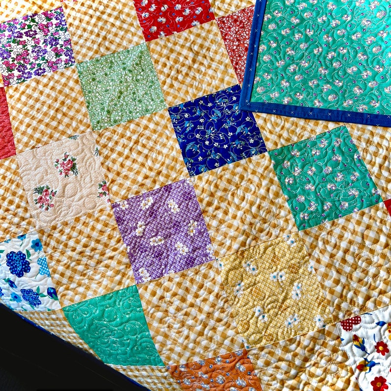 May include: A patchwork quilt featuring a range of floral and geometric designs in shades of blue, green, red, and yellow. The quilt is constructed from squares and rectangles, and the fabric is quilted with a diamond pattern.