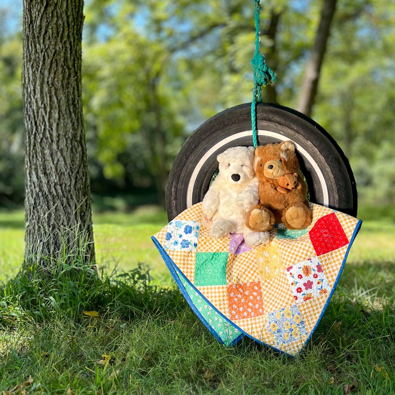 May include: Two stuffed toys, a brown bear and a white polar bear, are sitting on a yellow and green patchwork quilt. The quilt is draped over a tyre swing.