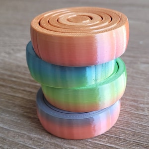 Puede incluir: Una pila de tres posavasos redondos de madera, coloridos e iridiscentes. El posavasos superior tiene un diseño de círculos concéntricos.