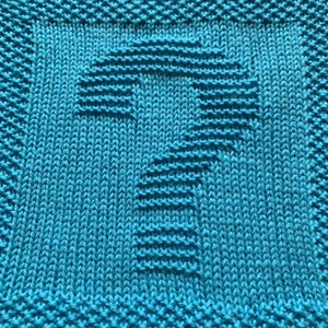 May include: A close-up of a knitted square in a vibrant turquoise colour. The square features a raised, textured design of the number one. The edges of the square have a decorative border, adding to the handmade aesthetic.