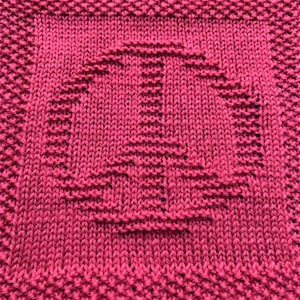 May include: A close-up of a knitted dishcloth in a deep pink color. The cloth has a textured pattern with a geometric design.