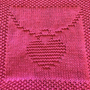 Könnte beinhalten: Ein rosa gestrickter Geschirrtuch mit einem Herz-Design in der Mitte.