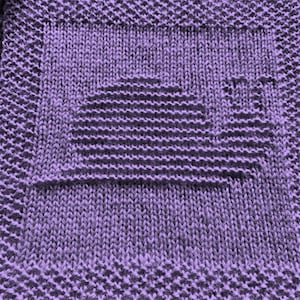 May include: A close-up of a purple knitted fabric with a square pattern. The fabric is made with a simple knit stitch and has a subtle texture.