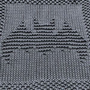 May include: A close-up of a gray knitted dishcloth with a geometric pattern. The dishcloth is made of a soft, absorbent material and is perfect for cleaning dishes or wiping down surfaces.