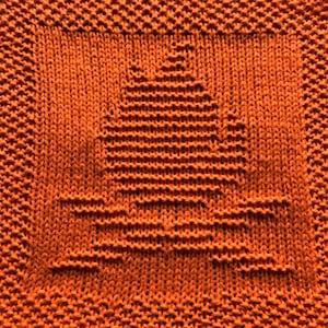 May include: A close-up of an orange knitted dishcloth with a simple geometric design in the center.