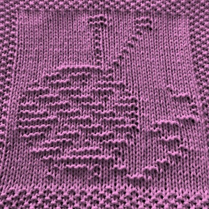 May include: A close-up of a knitted dishcloth in a light purple color. The cloth has a textured pattern.