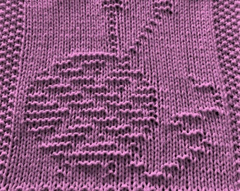 May include: A close-up of a knitted dishcloth in a light purple color. The cloth has a textured pattern.