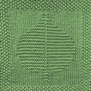 May include: Close-up of a knitted square in a light green color. The square features a detailed tree design in a darker shade of green, with a textured appearance. The tree is centered within the square, showcasing a detailed leaf pattern.