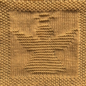 May include: A close-up of a knitted dishcloth in a mustard yellow color. The dishcloth has a woven pattern with a square design in the center.