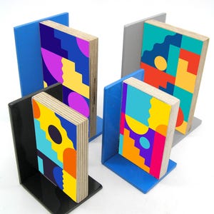 May include: Set of four bookends with colorful geometric designs. The bookends have a wooden appearance with vibrant patterns in blue, yellow, purple, orange, and teal. Two bookends are black, one is gray, and two are blue.