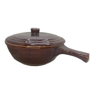 May include: A brown ceramic casserole dish with a lid and handle. The dish features a decorative pattern around the base and a small knob on the lid. The handle is on the right side of the dish.