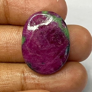 May include: An oval-shaped gemstone with a deep magenta hue, accented by patches of green. The polished surface reflects light, highlighting the stone's natural patterns. This gemstone is likely a ruby, suitable for jewelry.