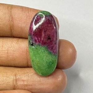 May include: An oval-shaped gemstone with a vibrant color split. The top half is a deep, rich red, transitioning to a bright green on the bottom. The polished surface reflects light, highlighting the natural patterns.