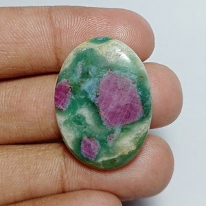 May include: Oval-shaped gemstone with a green base and vibrant pink inclusions. The stone has a polished surface, showcasing the natural patterns and colors. The gemstone is held in a hand, highlighting its size and shape.