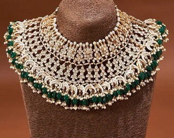 May include: A wide, ornate gold-tone choker necklace featuring intricate filigree metalwork, embedded clear stones, and small white pearl accents. The lower edge is finished with a fringe of dangling dark green beads and tiny white pearls.