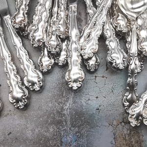 May include: A collection of ornate silver cutlery, including forks, knives, and spoons, with intricate designs and a polished finish.