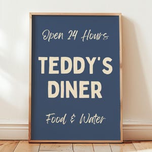 以下が含まれることがあります： 紺色の背景に「Open 24 Hours」、「TEDDY'S DINER」、「Food & Water」とクリーム色のフォントで書かれた額入りのサイン。 フレームは明るい茶色です。