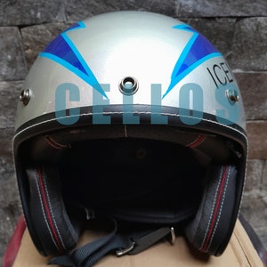 Op de afbeelding: Een zilverkleurige open motorhelm met blauwe bliksemschichtafbeeldingen aan de zijkanten en de tekst ICELLOS op de voorzijde. De helm is voorzien van drie metalen drukknopen aan de bovenrand en zwarte binnenvoering met rode stiksels.