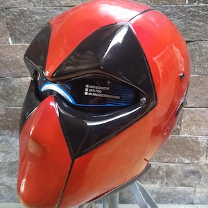 Könnte beinhalten: Ein rot-schwarzer Motorradhelm mit glänzendem Finish. Der Helm hat schwarze Akzente um die Augenpartie und einen roten Kinnbereich. Auf dem Visier steht "ANTI SCRATCH", "ANTI FOG" und "UV PROTECTION FILTER".