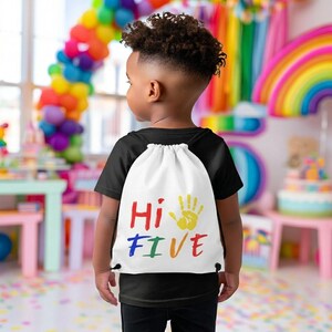 May include: A white drawstring backpack featuring the colorful text "Hi FIVE" and a yellow handprint graphic. The bag is worn over a black t-shirt, showcasing a vibrant design with red, blue, green, and yellow lettering against a plain white fabric.