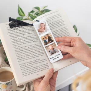 May include: A personalised bookmark with three photo slots and a black tassel. The bookmark features three family photos and the text "Happy Birthday Daddy xxx". The bookmark is held open in a book.