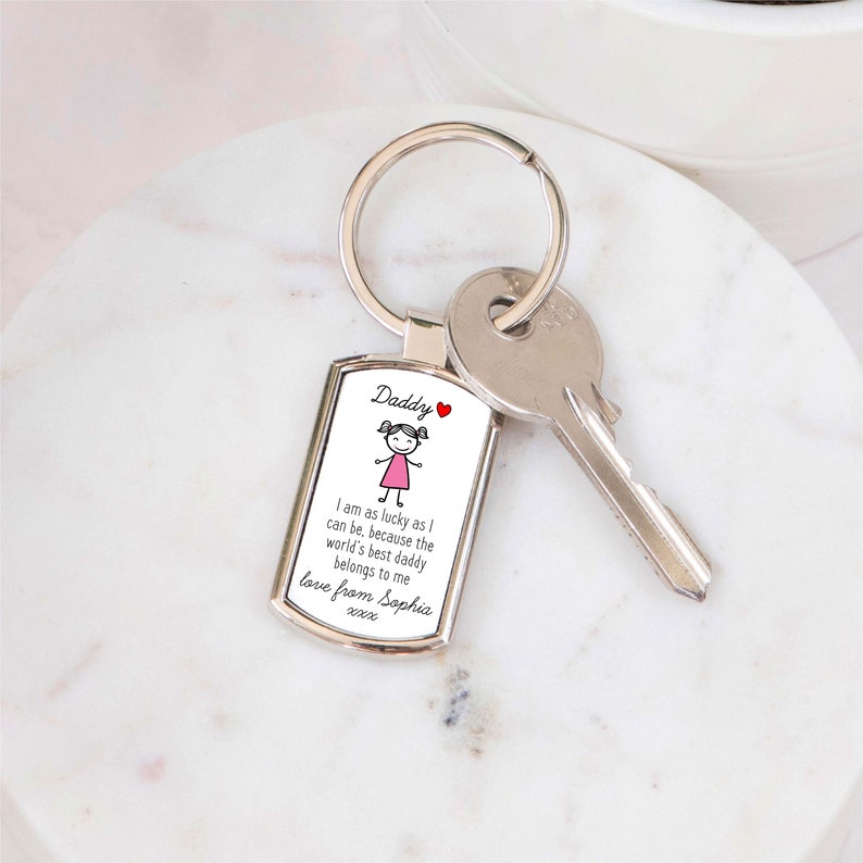 May include: Silver keychain with a white rectangular tag that says "Daddy" and features a cartoon girl in a pink dress. The tag also includes the text "I am as lucky as I can be, because the world's best daddy belongs to me love from Sophia xxx".