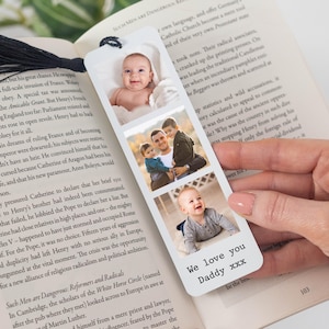 May include: A white bookmark with three family photos and the text "We love you Daddy xxx". The bookmark is held over an open book. The bookmark is a sentimental gift.