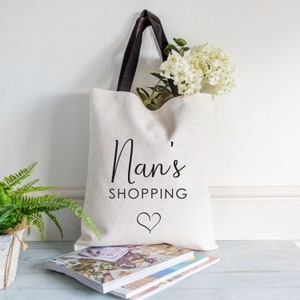 May include: A white canvas tote bag with black handles and the text "Nan's Shopping" with a heart underneath.
