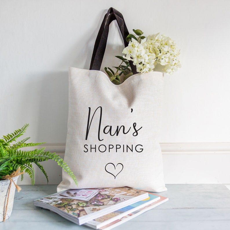 May include: A white canvas tote bag with black handles and the text "Nan's Shopping" with a heart underneath.