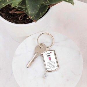May include: A silver keychain with a rectangular charm that says "Daddy I am as lucky as I can be, because the world's best daddy belongs to me love from Olivia". The charm has a small cartoon drawing of a girl with pink hair and a pink dress.