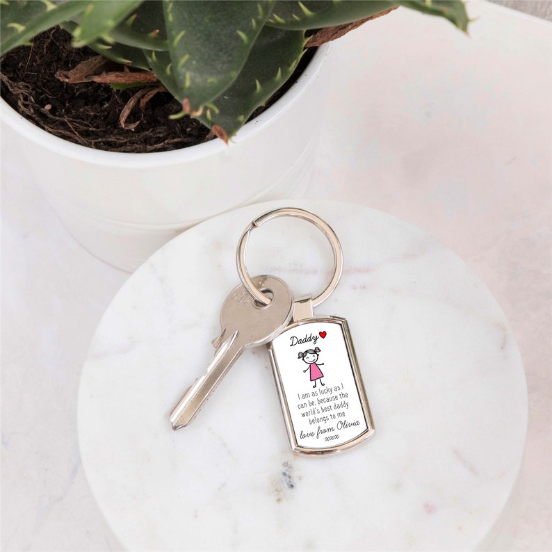 May include: A silver keychain with a rectangular charm that says "Daddy I am as lucky as I can be, because the world's best daddy belongs to me love from Olivia". The charm has a small cartoon drawing of a girl with pink hair and a pink dress.