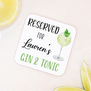 May include: White square coaster with the text "Reserved for Lauren's Gin & Tonic" in black and green lettering. A watercolor illustration of a gin and tonic drink with a lime wedge and mint sprig is on the right side of the coaster.