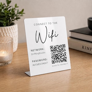 May include: A white rectangular acrylic sign with black text and a QR code. The sign reads CONNECT TO THE Wifi, NETWORK: DriftingDucks, PASSWORD: AbCdE1234567, and SCAN TO CONNECT. It features a bent base for standing upright on a flat surface.