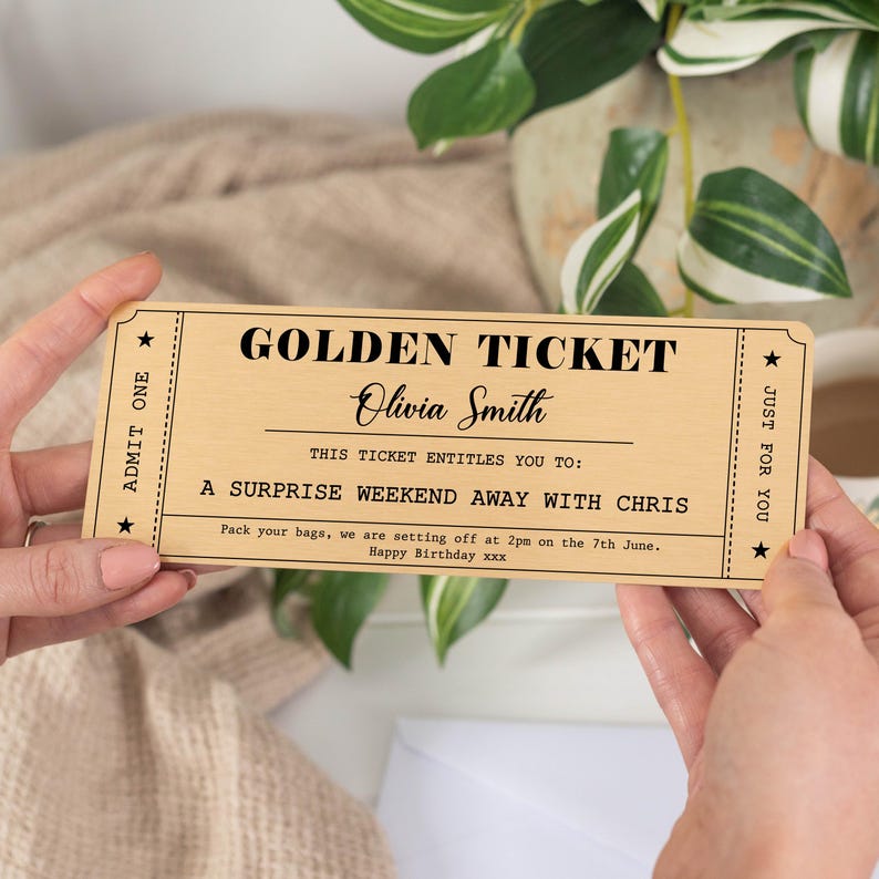Puede incluir: Un "Golden Ticket" de madera con texto negro, sostenido por manos. El billete dice "Golden Ticket" y "Olivia Smith", prometiendo un fin de semana sorpresa. El texto tambi&eacute;n incluye la fecha y hora del viaje.