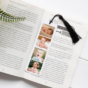 May include: A white rectangular bookmark featuring four vertical photographic portraits of a child at different ages, ranging from infancy to toddlerhood. The bookmark is topped with a black fabric tassel and is placed inside an open book.