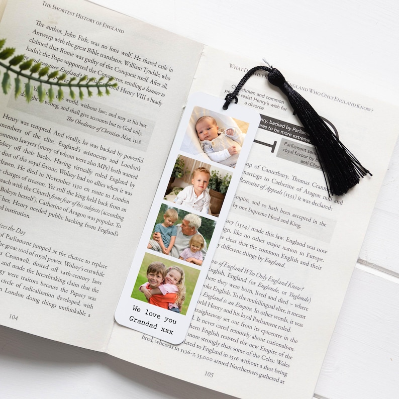 May include: A bookmark with four family photos and a black tassel, placed in a book. The bookmark has the text "We love you Grandad xxx" at the bottom. The book is open to page 104.