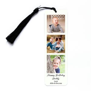 May include: A white bookmark with three family photos and a black tassel. The bookmark has the text "Happy Birthday Daddy, Love, Alfie & Eva xxx" in black script. The photos show a baby, a family, and a young girl.